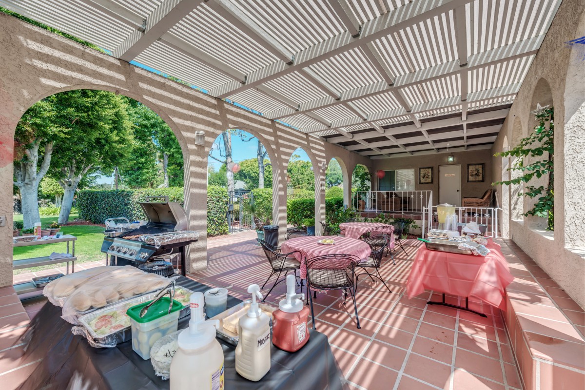 An inviting outdoor patio setup with tables, chairs, and a BBQ grill under a pergola.