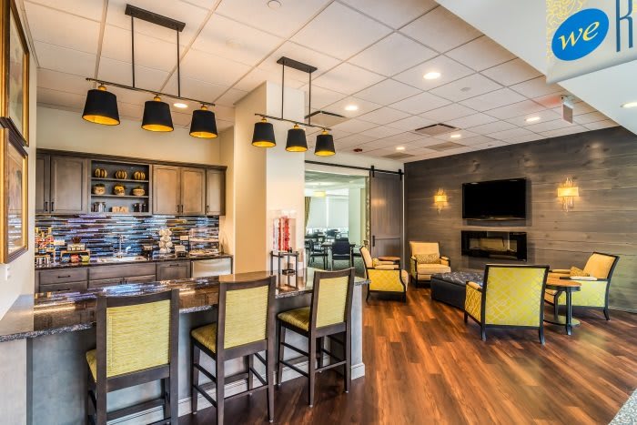 A modern lounge area featuring a stylish bar with high chairs, comfortable seating, and a wall-mounted television.