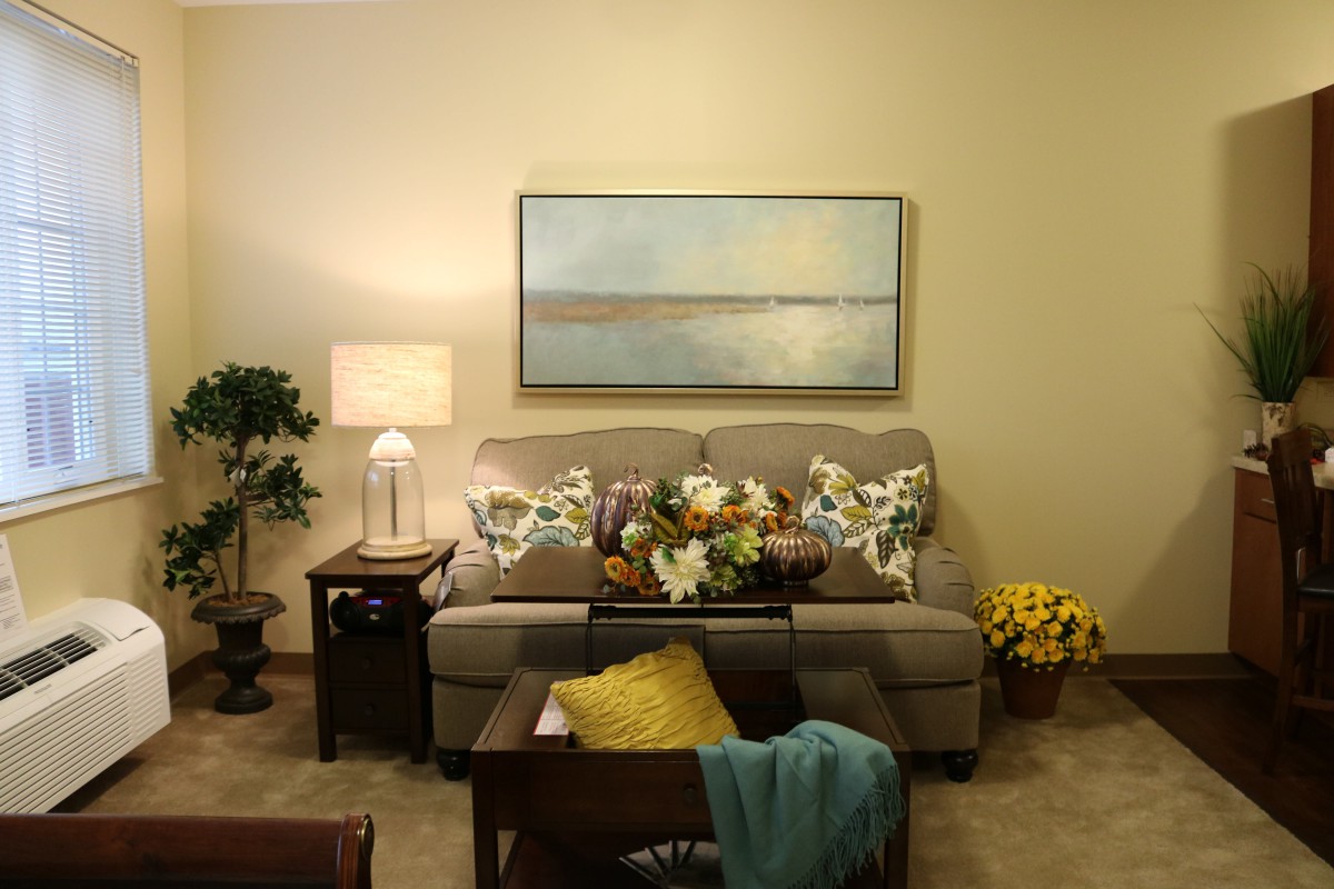 A cozy living room with a sofa adorned with floral cushions, a lamp on a side table, and artwork on the wall.