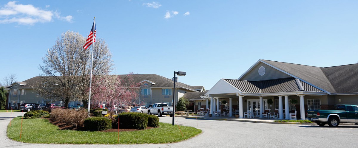 A residential building with a parking lot and landscaped surroundings under a clear blue sky.