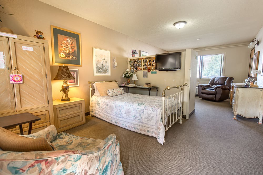 A cozy bedroom featuring a single bed, artwork on the walls, and a TV mounted on the wall.