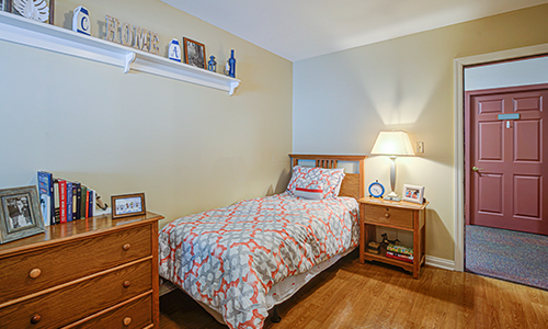A cozy bedroom with a single bed and warm lighting, featuring wooden furniture and decorative elements.