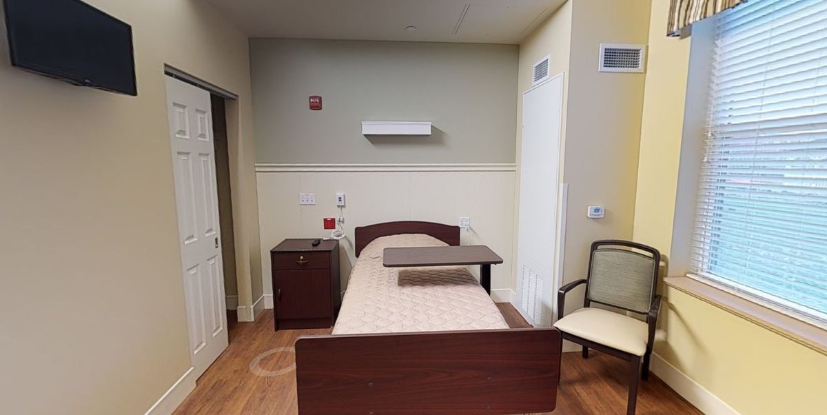 A simple hospital room with a single bed, nightstand, and chair.