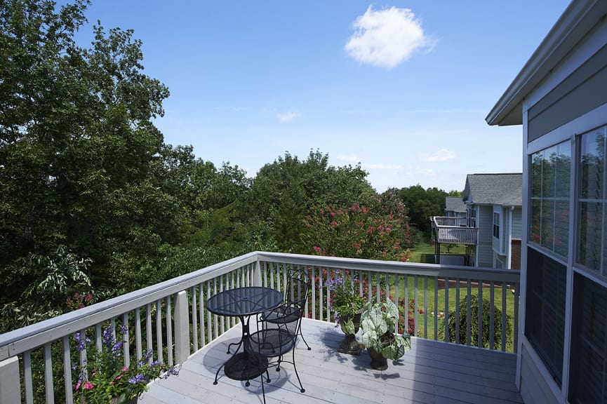 A peaceful outdoor deck with a table and chairs, surrounded by lush greenery under a clear blue sky.