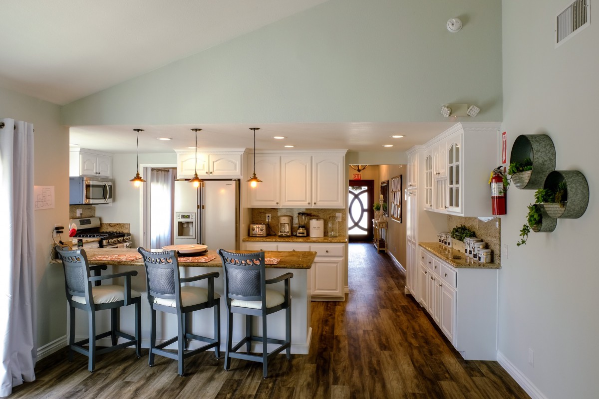 A modern kitchen with white cabinets, pendant lighting, and wooden flooring.