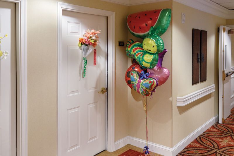 A hallway with a decorated door featuring a bouquet of flowers and colorful balloons.