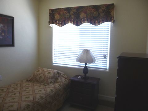 A cozy bedroom with a bed, nightstand, lamp, and a window with blinds.