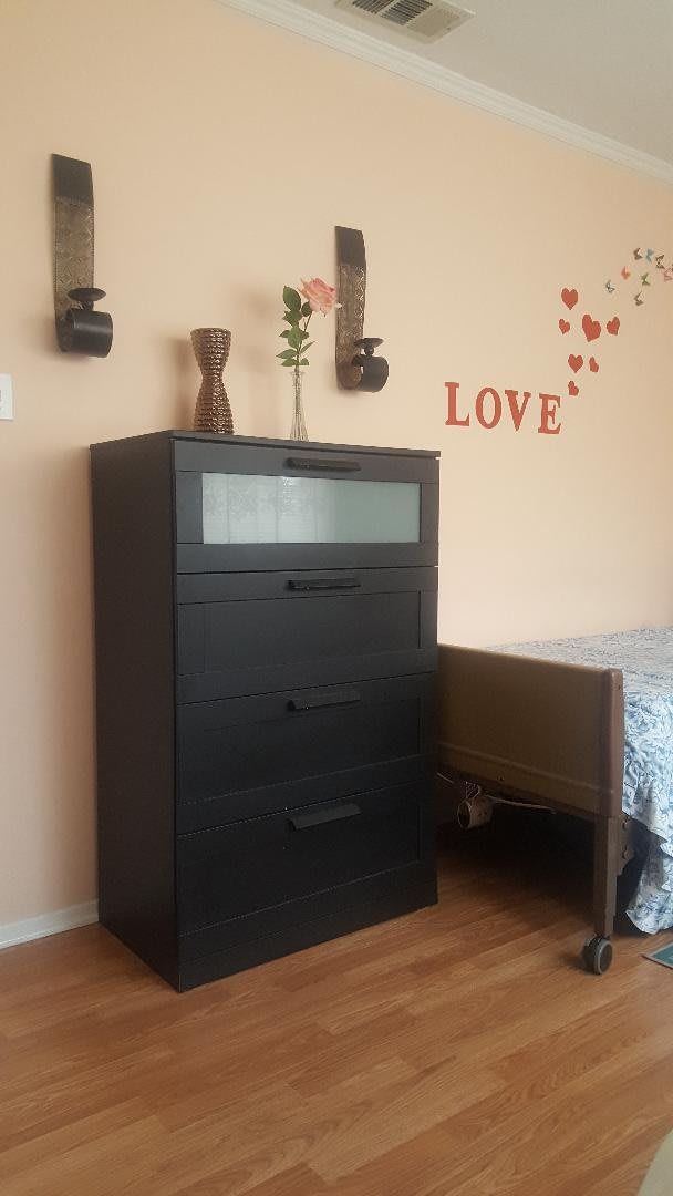 A cozy bedroom corner featuring a black dresser adorned with decorative items and a love-themed wall decal.