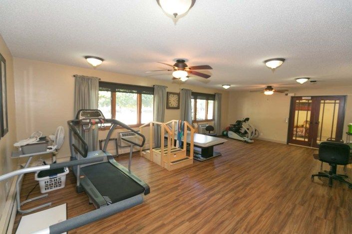 A spacious fitness room with gym equipment including a treadmill and exercise bike, featuring wooden flooring and ceiling fans.