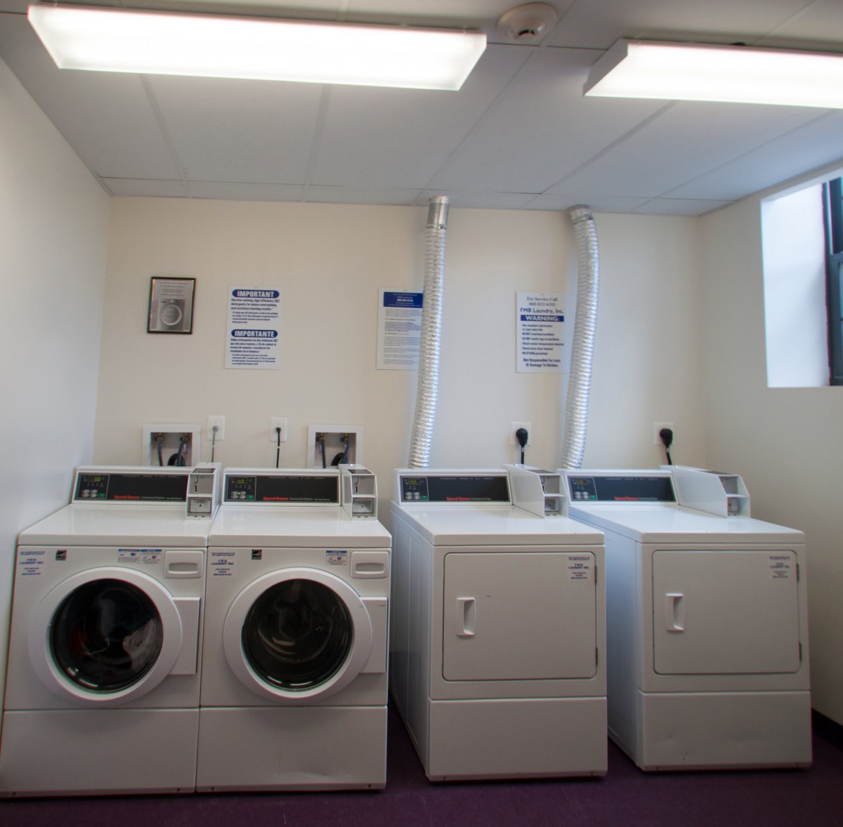 A laundry room featuring two washing machines and two dryers side by side.