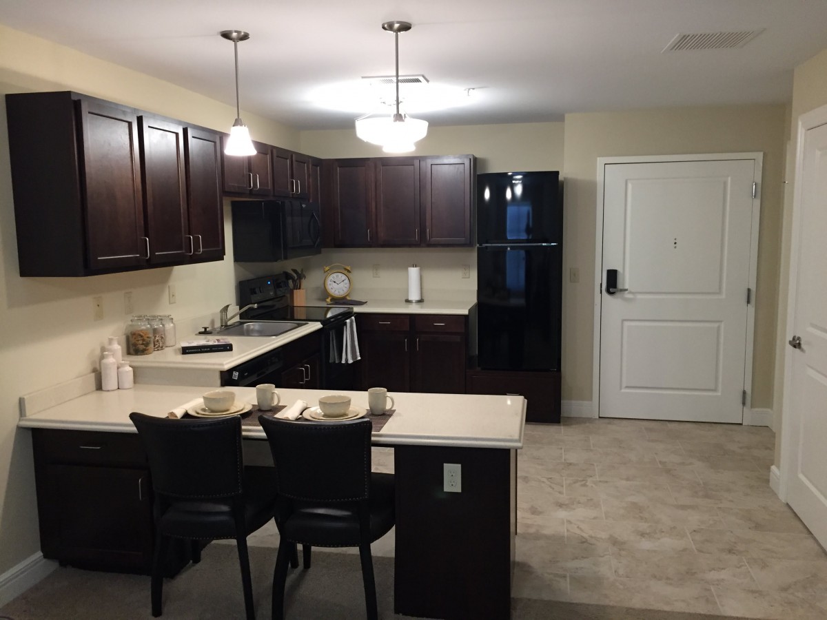 A modern kitchen with dark cabinets, a small dining area, and pendant lighting.