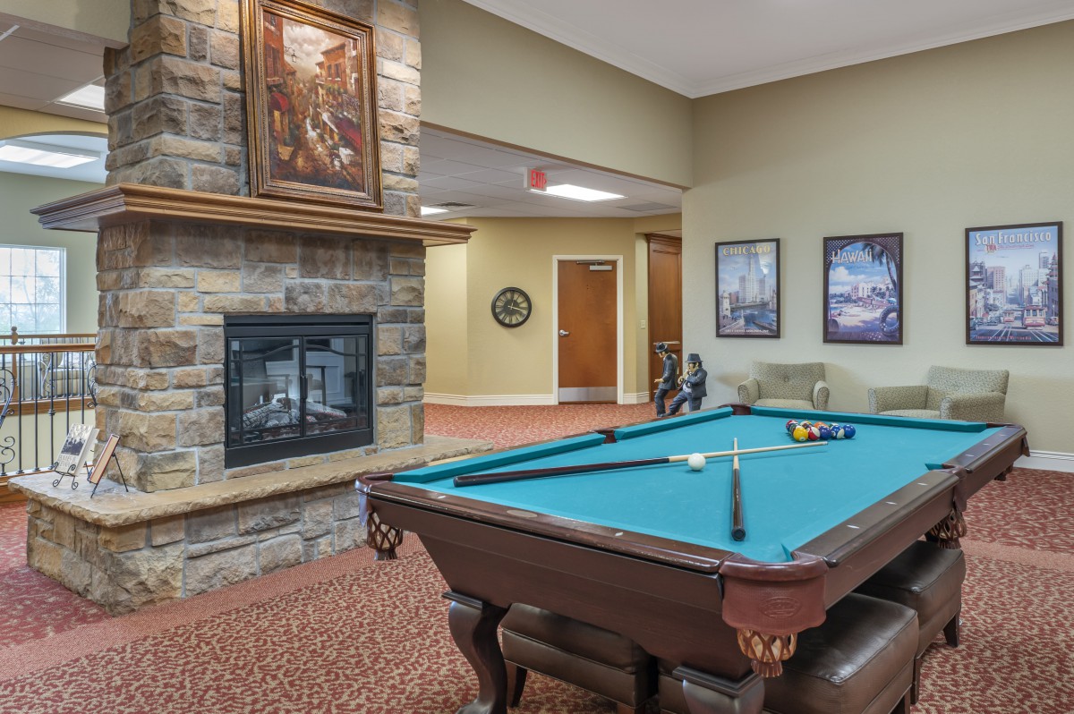 A cozy game room featuring a pool table and a stone fireplace.