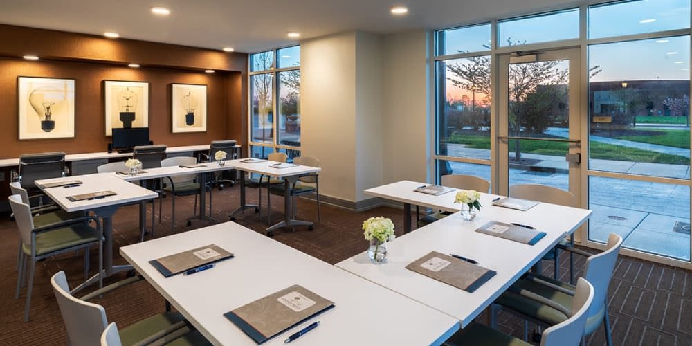 A modern conference room set up with tables, notepads, and flowers, illuminated by natural light from large windows.