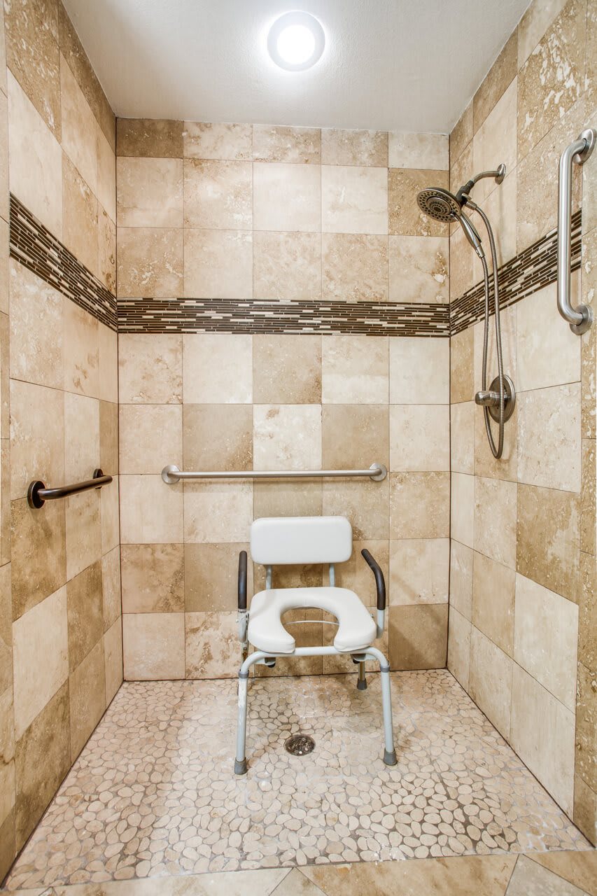 A modern accessible shower with a chair and safety grab bars.