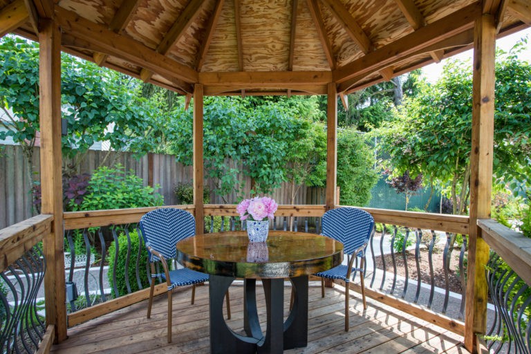 A cozy gazebo with a table and two chairs set amidst a lush garden.