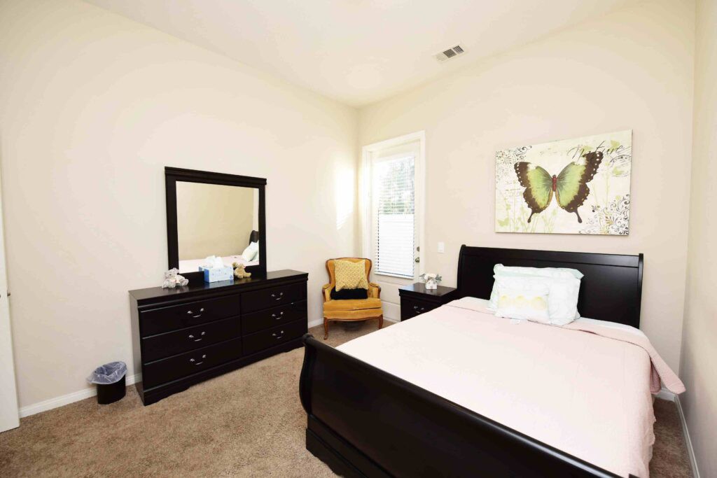 A neatly arranged bedroom with a bed, dresser, mirror, and artwork.