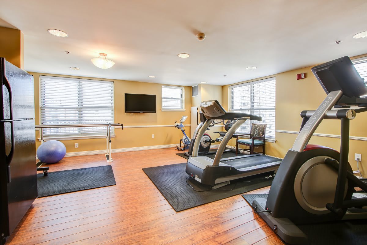 A well-lit gym with treadmills and exercise equipment on a hardwood floor.