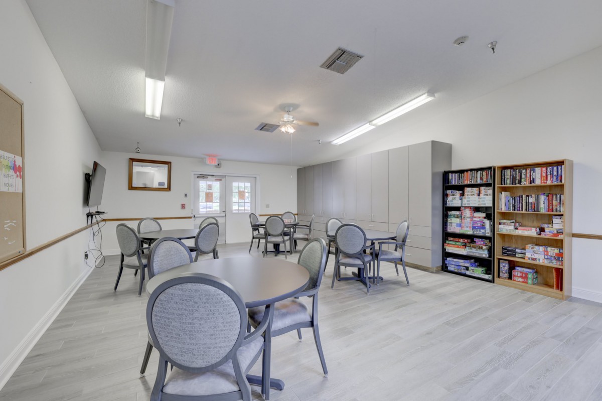 A community room with tables, chairs, and a bookshelf under bright lighting.