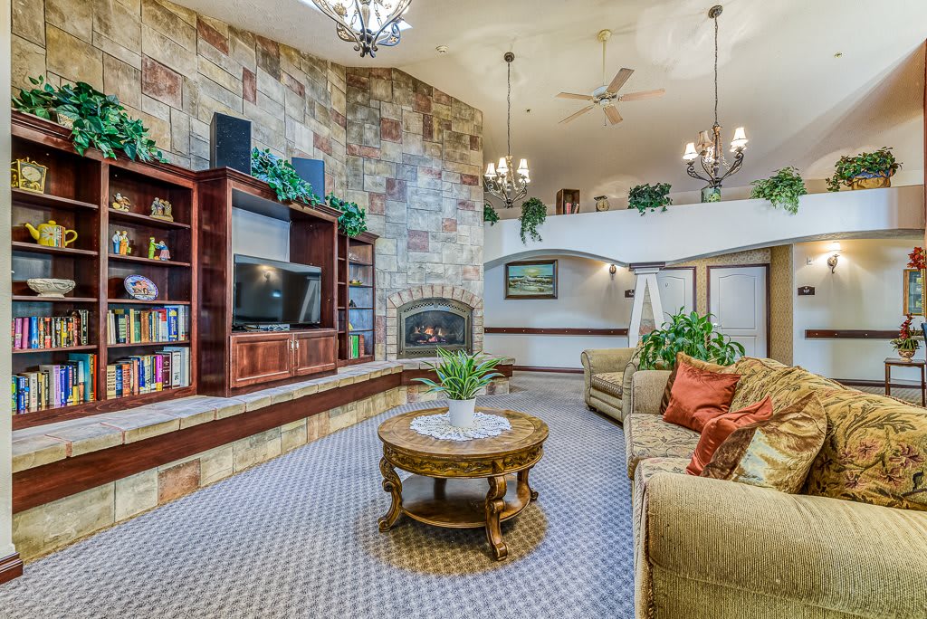 A cozy living room featuring a stone accent wall with built-in shelves, a fireplace, chandeliers, and comfortable seating.