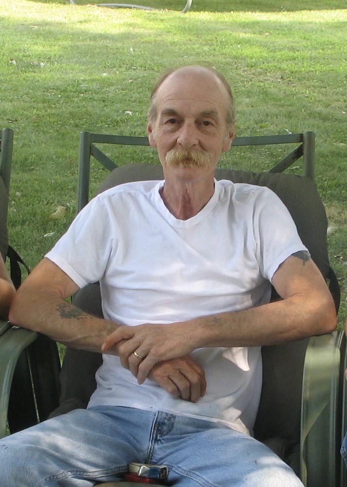 A man sitting casually outdoors on a chair.