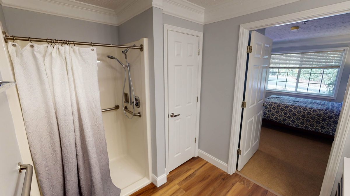 A modern bathroom with a shower and hardwood flooring, featuring two doors leading to adjacent rooms.