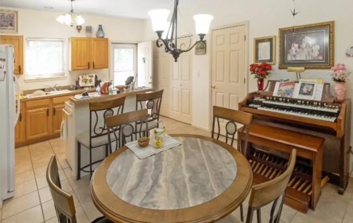 A cozy dining area with a round table, wooden chairs, and a view into the kitchen, featuring a vintage piano in the corner.
