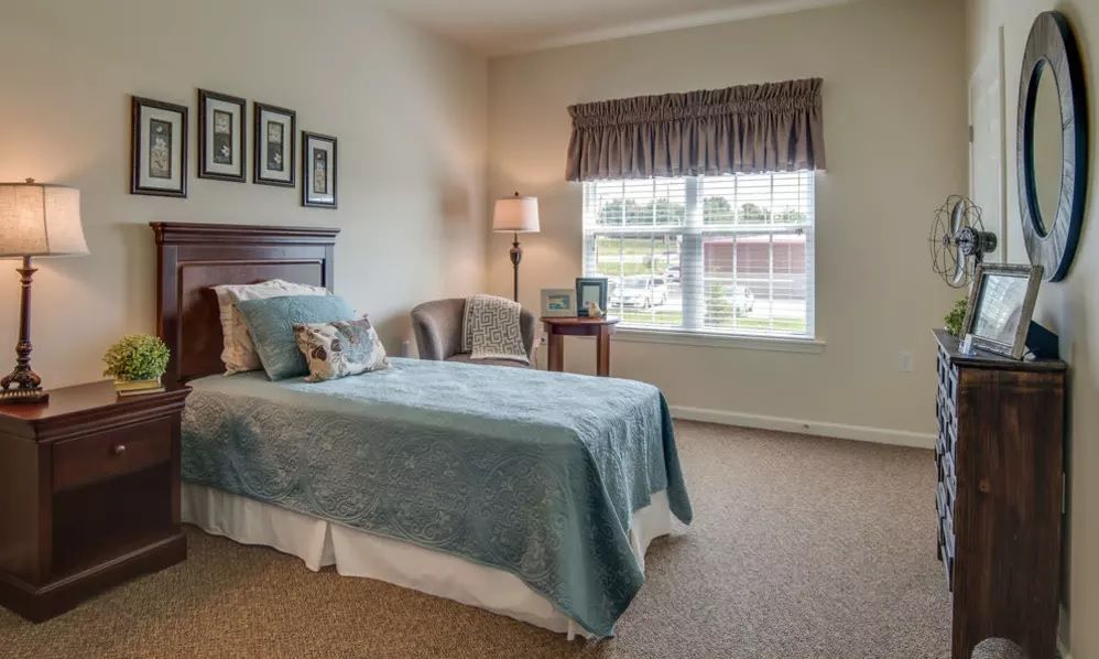 A cozy bedroom with a single bed, carpeted floor, and natural light coming through the window.
