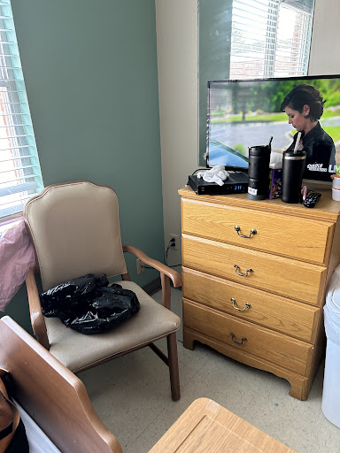 A cozy room featuring a chair, dresser, and a television displaying a scene.