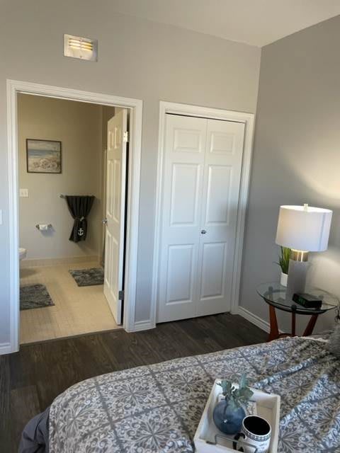 A cozy bedroom with a bed, nightstand, lamp, and a view into an adjoining room through an open doorway.