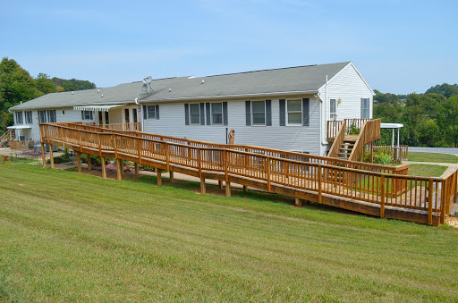 A wooden ramp leads up to a single-story building, surrounded by green grass and under a clear blue sky.