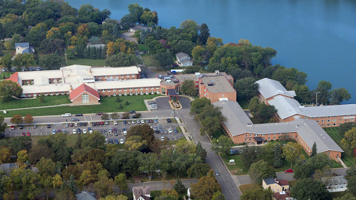 An aerial view of a school campus surrounded by lush greenery and a serene lake.