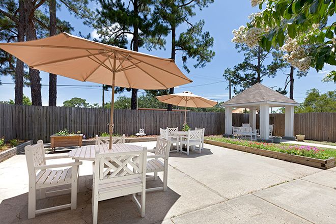 A sunny outdoor patio area with tables, chairs, and umbrellas surrounded by trees.