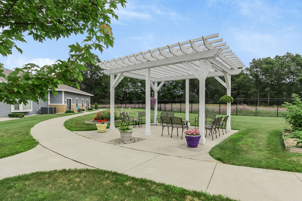 A white pergola with seating in a landscaped garden setting.