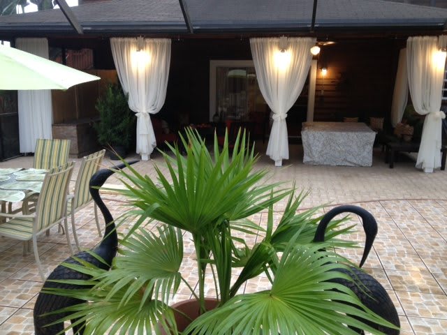 A relaxing outdoor patio with lush greenery and elegant white curtains.