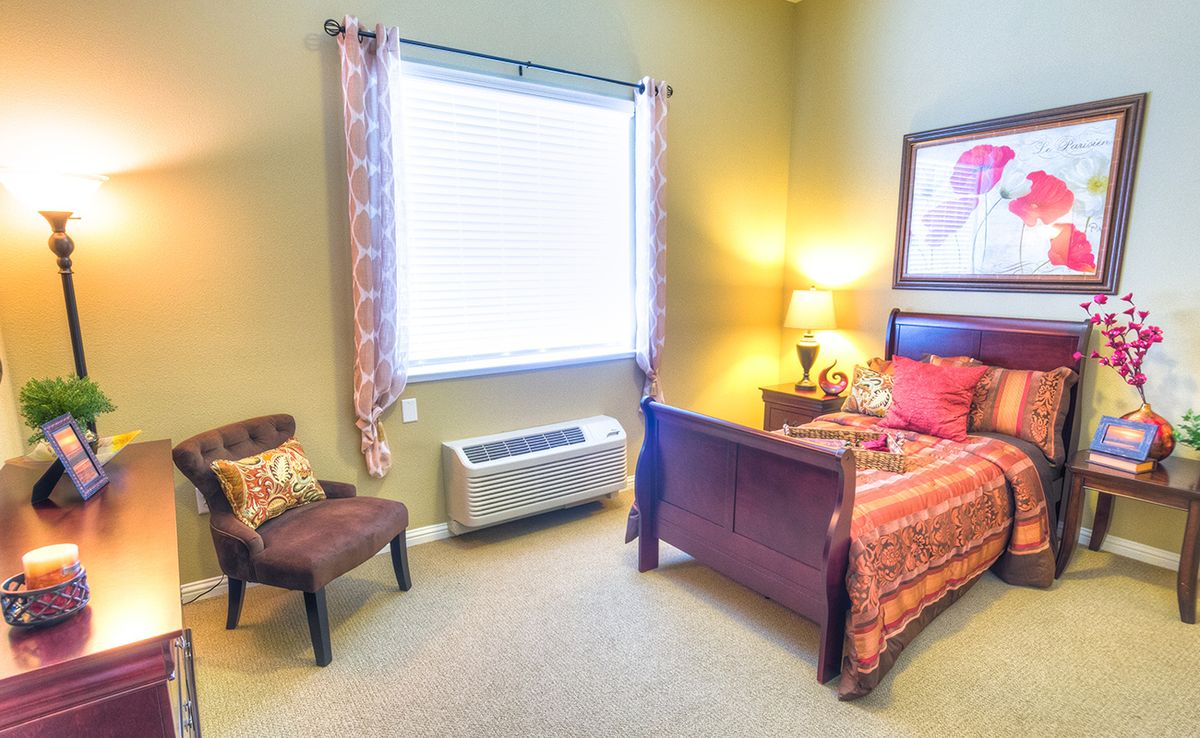 A cozy bedroom with a bed, chair, and window letting in natural light.