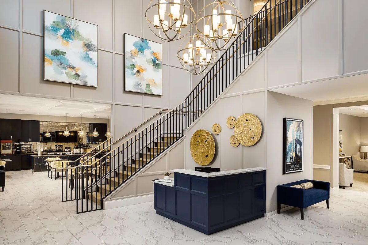 A modern lobby with elegant chandeliers, a grand staircase, and contemporary artwork.