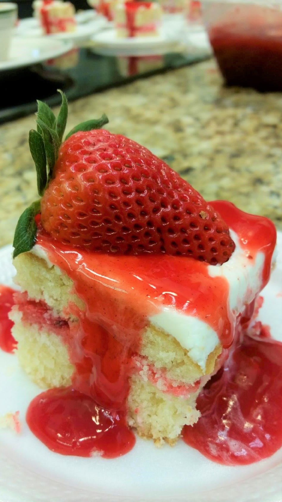 A slice of cake topped with a fresh strawberry and drizzled with red syrup.