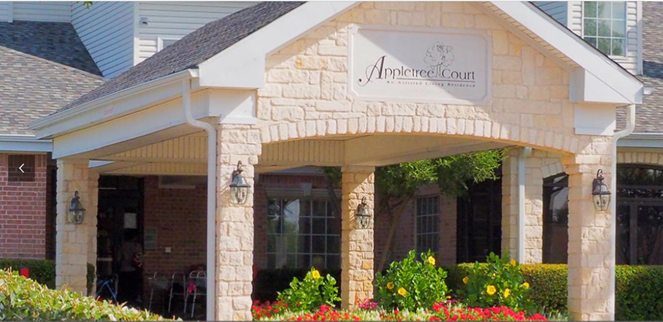 The entrance to a building with stone columns and landscaped flowers.