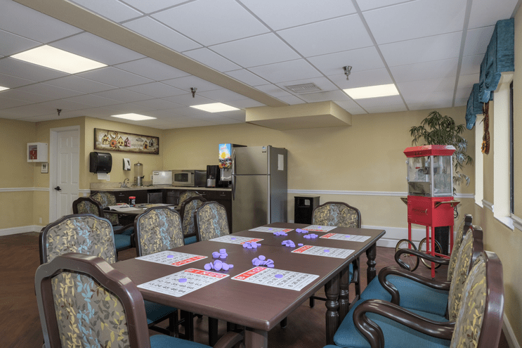A dining area with a kitchen setup, featuring tables and chairs, a refrigerator, and a popcorn machine.