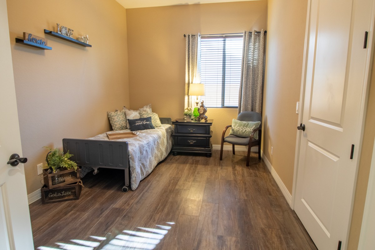 A cozy bedroom with a single bed, nightstand, and a chair by the window.