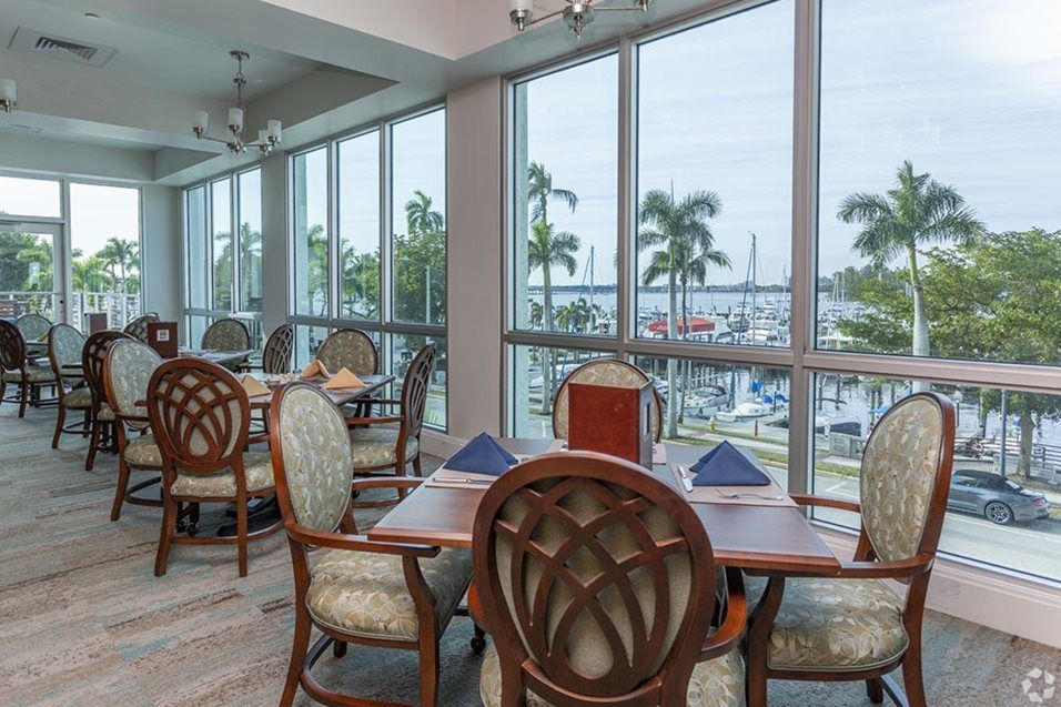 A well-lit restaurant dining area with large windows offering a view of palm trees and the outdoors.