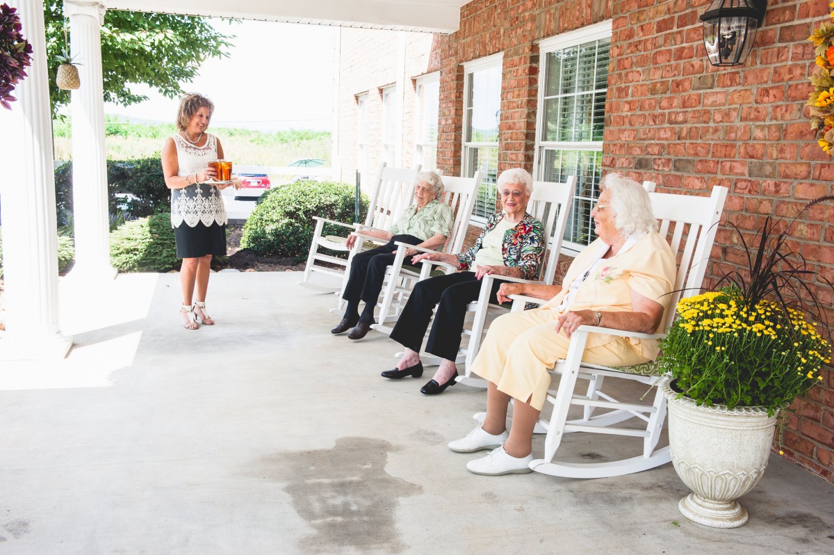 A group of seniors relaxing on a porch in rocking chairs, enjoying each other's company.