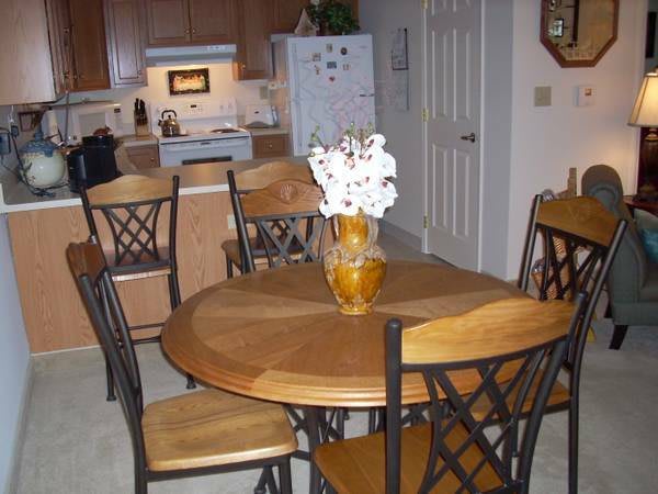 A cozy kitchen dining area with a wooden table and chairs, featuring a vase of flowers.