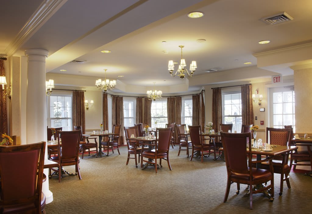 An elegant dining room with neatly arranged tables and chairs, illuminated by chandeliers.