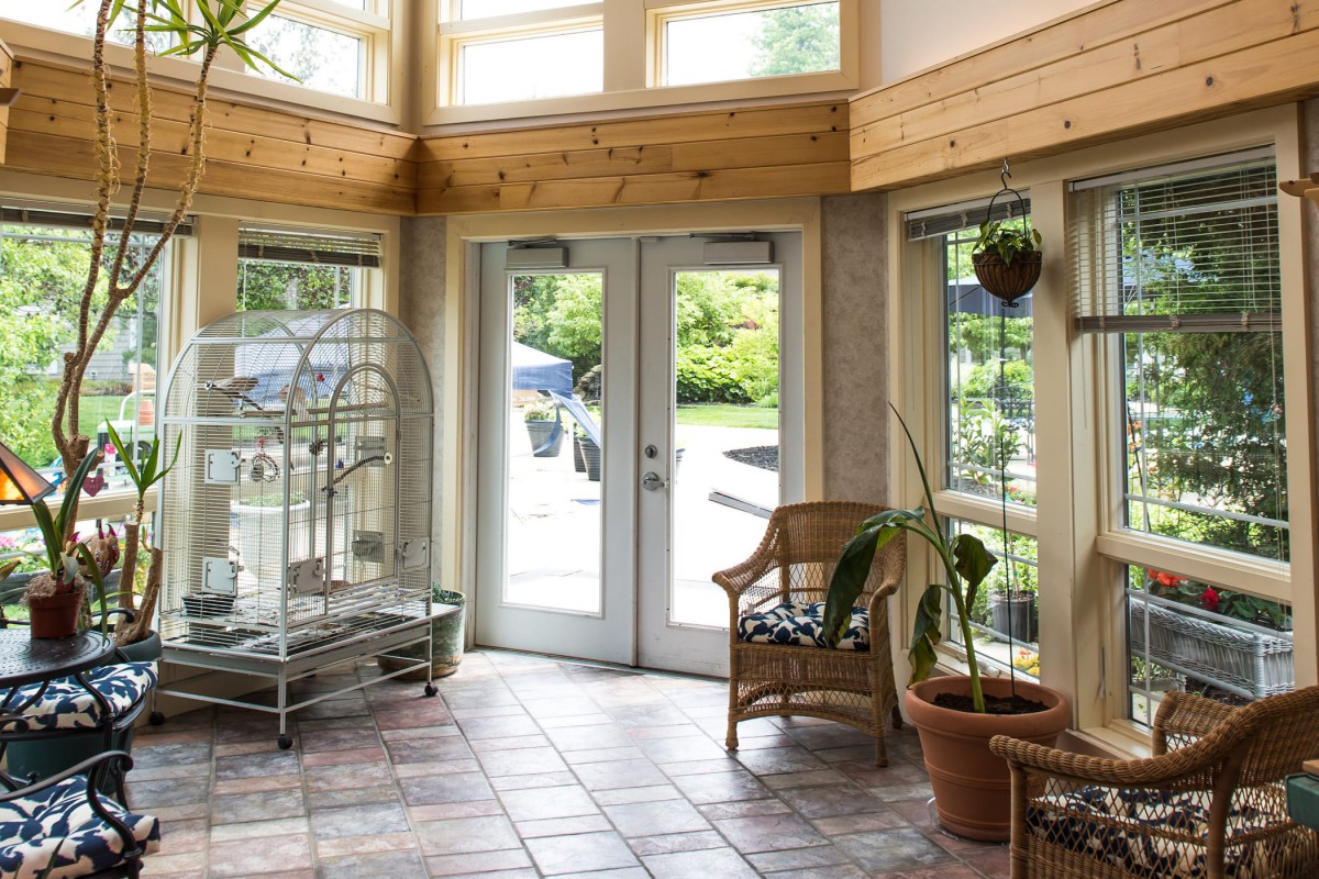 A bright sunroom with large windows, plants, and tiled flooring.