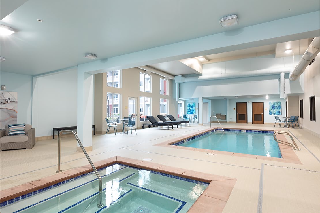An inviting indoor spa area featuring a swimming pool, hot tub, and lounge chairs.
