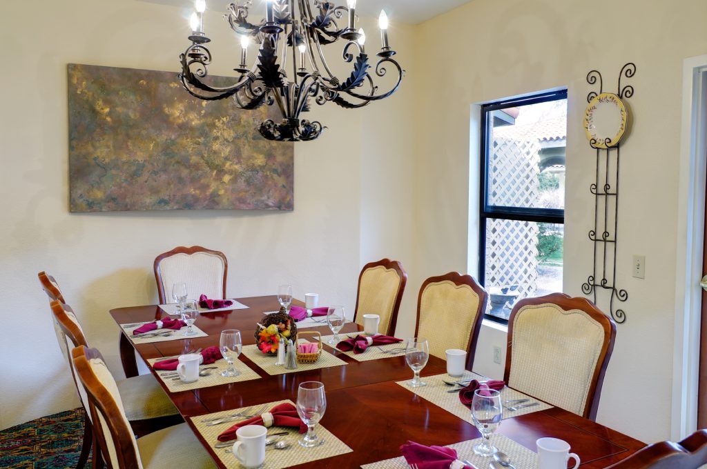 An elegant dining room with a chandelier, set for a meal with neatly arranged tableware and chairs.