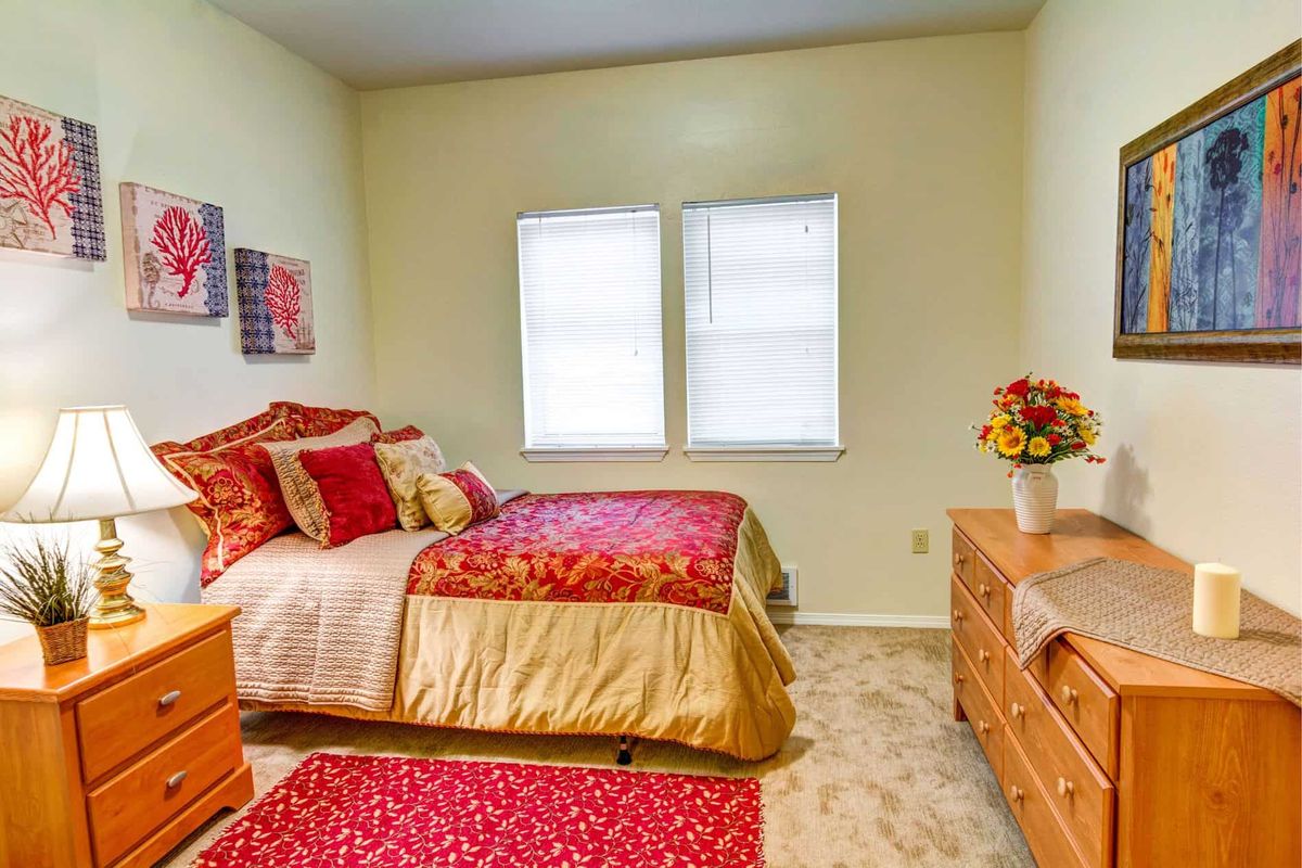 A cozy bedroom with colorful bedding, two windows, and wooden furniture.