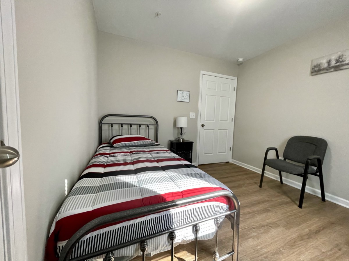 A minimalist bedroom with a single bed, chair, and nightstand.