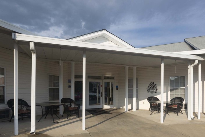 A white building entrance with columns and outdoor seating under a cloudy sky.